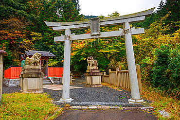 Traditional Shinto torii gate with guardian lion-dog statues surrounded by autumn foliage on Mount Hiei, near Kyoto, Japan.