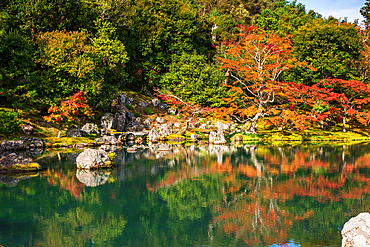 Autumn trees reflecting on a tranquil pond surrounded by rocks in the gardens of Tenryū-ji Temple, Kyoto, Japan