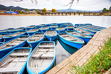 A fleet of blue rowboats docked on the serene Arashiyama River in Kyoto, surrounded by scenic autumn landscapes.