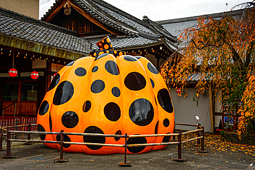 A vibrant pumpkin sculpture by Yayoi Kusama displayed outside a Kyoto temple, blending contemporary art with traditional surroundings.