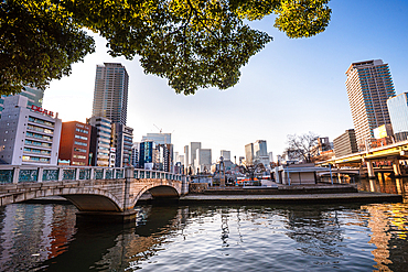 Nakanoshima in Osaka, Japan. A green Island park in the center of Osaka. Beautiful stone bridge over the river opening the view to downtown highrise buildings.