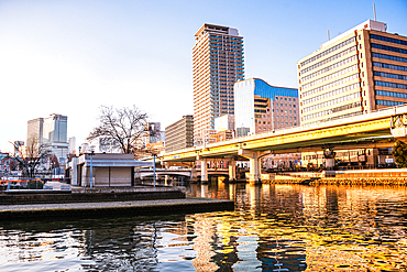 Reflecting golden light on Dojima River at Nakanoshima in Osaka, Japan. A green Island park in the center of Osaka. Highrise building ans bridges