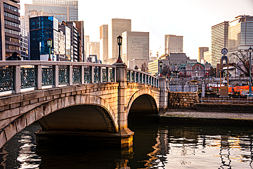 Pucturqesque Barazono bashi bridge in front of towering skyscrapers in golden evening lights. Nakanoshima in Osaka, Japan. A green Island park in the center of Osaka.