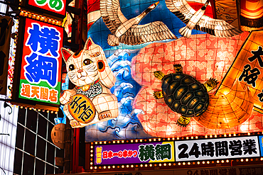 A vibrant, illuminated Japanese signboard featuring a lucky cat, turtle, cranes, and traditional motifs, seen in the lively streets of Osaka. Shinsekai, Osaka, Kansai, Japan