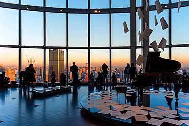 Panoramic view through a big window in Roppongi Hills, with visitors enjoying the evening light, silhouettes and grand piano, Tokyo, Honshu, Japan, Asia