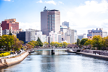 Motoyasu Bridge and Hiroshima cityscape on a bright day with reflections on the river and people walking along the promenade