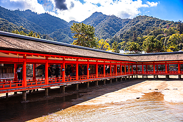 Covered Wooden Corridor of Itsukushima Shrine Framed by Lush Mountains on Miyajima Island, Japan