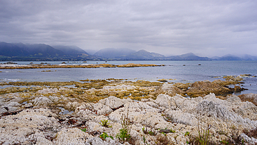 Tidal rocky flats and calm sea with distant mountains at Kaikoura Peninsula, South Island, New Zealand