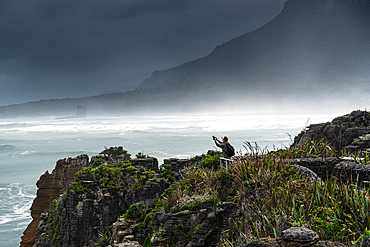 Tourist Taking a Selfie on Windy Cliff Edge Above Crashing Surf at Pancake Rocks, Punakaiki, Paparoa National Park, West Coast, New Zealand