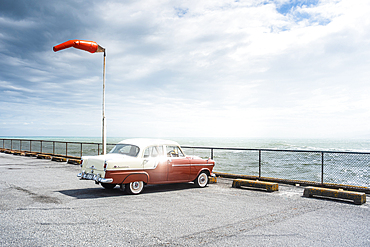 Classic Red Car Parked by the Sea with Windsock Blowing on Windy Day at West Coast Lookout, New Zealand