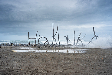 Driftwood Sculpture Spelling “Hokitika” on Misty Beach with Reflections on Wet Sand, West Coast, New Zealand