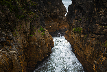 Narrow Chasm with Surging Ocean Waves Between Sheer Cliffs at Pancake Rocks, Punakaiki, West Coast