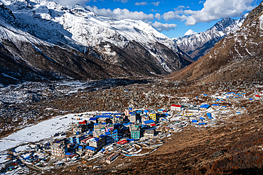 High-angle view of colorful buildings in Kyanjin Gompa village nestled in the snow-dusted Langtang Valley, surrounded by dramatic Himalayan peaks in Nepal