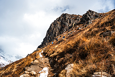 Narrow alpine trail winding along a steep hillside above Langtang Valley, leading toward the snowy ridgelines near Kyanjin Gompa, Nepal