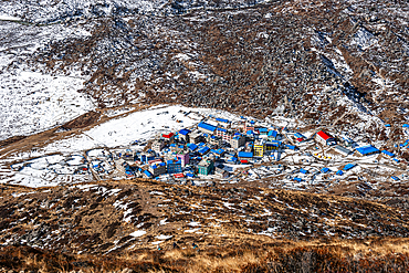 Colorful rooftops of Kyanjin Gompa nestled in a snowy Langtang Valley landscape, viewed from the trail to Kyanjin Ri