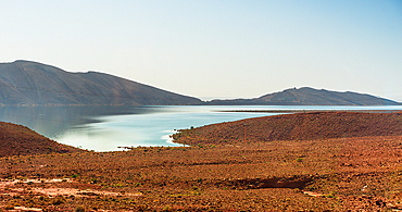 Narrow winding inlet of Barrage Al-Hassan Addakhil glistening between rolling red hills in Parc National Al Hassan Addakhil
