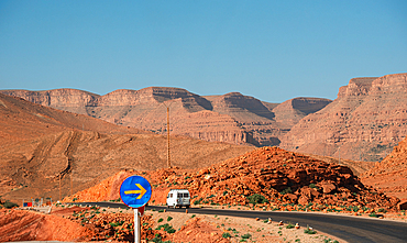 White van navigating a sharp desert road bend in Parc National Al Hassan Addakhil, red rocks and distant mountains under a clear blue sky