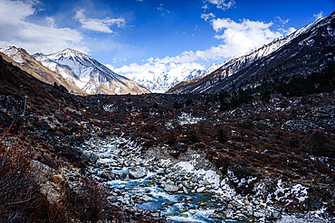 Meltwater stream winding through the alpin.e landscape of Langtang Valley with snowy peaks. Lang tang river and tserko with Gangchempo