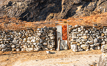 Stone wall and rustic wooden door set against sunlit mountainside in the remote village terrain of Langtang Valley, Nepal