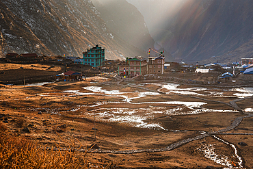 Langtang Village in soft morning light with scattered snow patches across terraced valley floor, traditional lodges, and rugged Himalayan backdrop