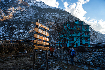 Backpackers arrive at Sunrise Guest House in Langtang Village, Nepal, with green-painted lodge and snow-dusted cliffs under blue sky