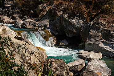 Turquoise mountain river cascading over smooth boulders in Langtang Valley, Nepal, surrounded by rocks and sparse dry vegetation