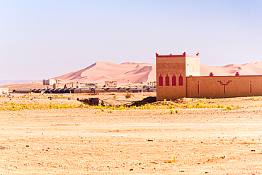 Isolated fortress-like desert building with palm groves and Erg Chebbi dunes beyond in Merzouga