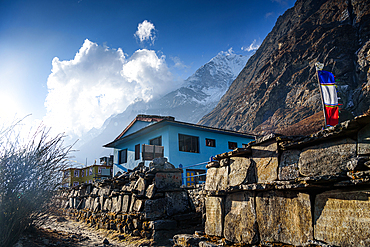 Blue teahouse and prayer flags under dramatic clouds along the trekking route in Langtang Valley, Nepal