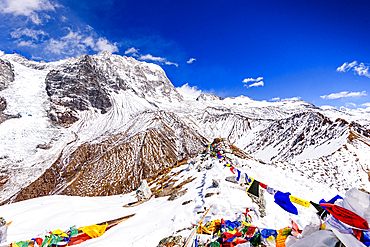 High-altitude view north from Kyanjin Ri summit with prayer flags and dramatic snow-covered ridges of Ubra and Kimshung, Nepal