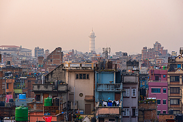 Dense urban skyline of Kathmandu at sunset with Dharahara Tower rising in the distance