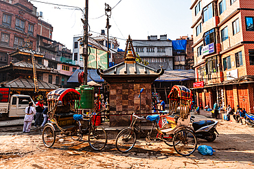 Small stupa surrounded by rickshaws and people in a Kathmandu street, blending religion and urban life