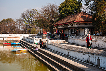 Women walking along the steps of a calm pond area surrounded by trees and heritage structures in Bhaktapur