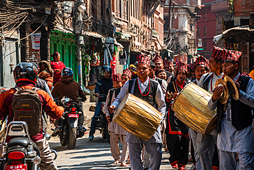 Traditional Nepali street procession with musicians carrying large drums through a narrow lane in Bhaktapur