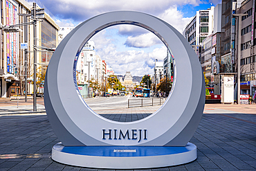 Modern circular Himeji city monument framing a view of the distant Himeji Castle along a wide pedestrian-friendly boulevard