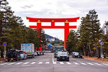 Red torii gate over a busy street filled with cars and lined with trees, leading toward Heian Shrine in Kyoto, Japan