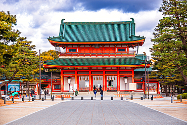 Front view of Heian Shrine’s vibrant red main gate with green-tiled roof and symmetrical design framed by pine trees in Kyoto, Japan