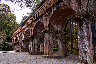 Historic red brick arches of the Suirokaku Aqueduct nestled among tall cedar trees in the temple grounds of Nanzen-ji, Kyoto