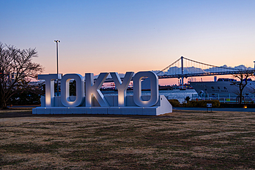 Sunset view of Tokyo’s iconic waterfront with large TOKYO sign in Odaiba and Rainbow Bridge spanning Tokyo Bay in the background