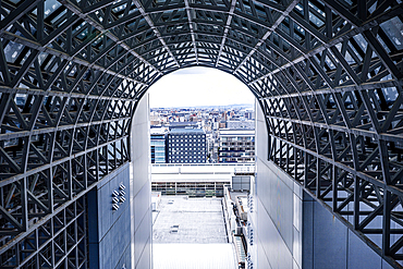 Futuristic steel and glass architecture of Kyoto Station's skywalk corridor with a cityscape view through the geometric frame