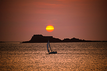 Sunset over the British Channel view from Saint Malo, Brittany France. Silhouette of Sailing boat in front of islands in the vibrant setting sun above Fort d'île Harbour
