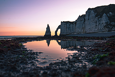 The dramatic chalk cliffs and natural arch of Étretat reflect in a tidal pool at sunrise on the Normandy coast of France. Aiguille d'Etretat, Falaise d‘Aval