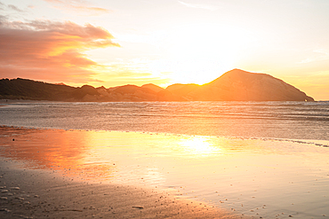 Fiery sunset reflects across the wet sands of Wharariki Beach on the South Island of New Zealand.