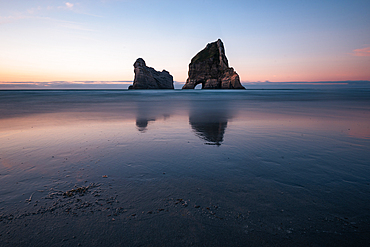 he Archway Islands silhouette against the glowing twilight sky at Wharariki Beach, Golden Bay, New Zealand.