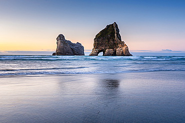 Sunset long exposure The Archway Islands reflect in wet sand at Wharariki Beach, Golden Bay, New Zealand.