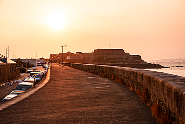 Golden sunset over the stone harbour walkway with Castle Cornet Rock in St Peter Port, Guernsey, Channel Islands.