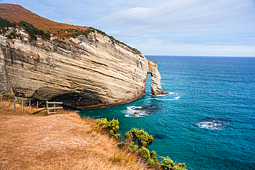 Striking sedimentary rock formations rise above turquoise waters at Cape Farewell, Golden Bay, New Zealand.