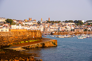 View across the harbour of St Peter Port with historic stone quay and marina at sunrise, Guernsey, Channel Islands, United Kingdom.
