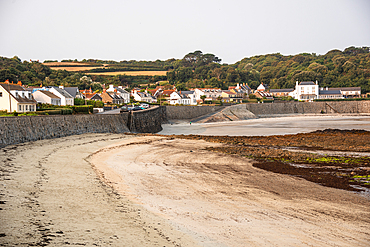 Traditional houses along the shoreline of Rocquaine Bay with stone seawall at low tide, Guernsey, Channel Islands, United Kingdom.