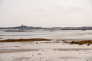 Expansive tidal flats exposed at low tide in Rocquaine Bay, with distant views of Guernsey’s coastline, Channel Islands, United Kingdom.