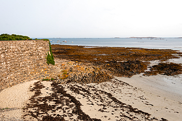 Coastal stone wall leading onto the sandy tidal flats of Rocquaine Bay, Guernsey, Channel Islands, United Kingdom.